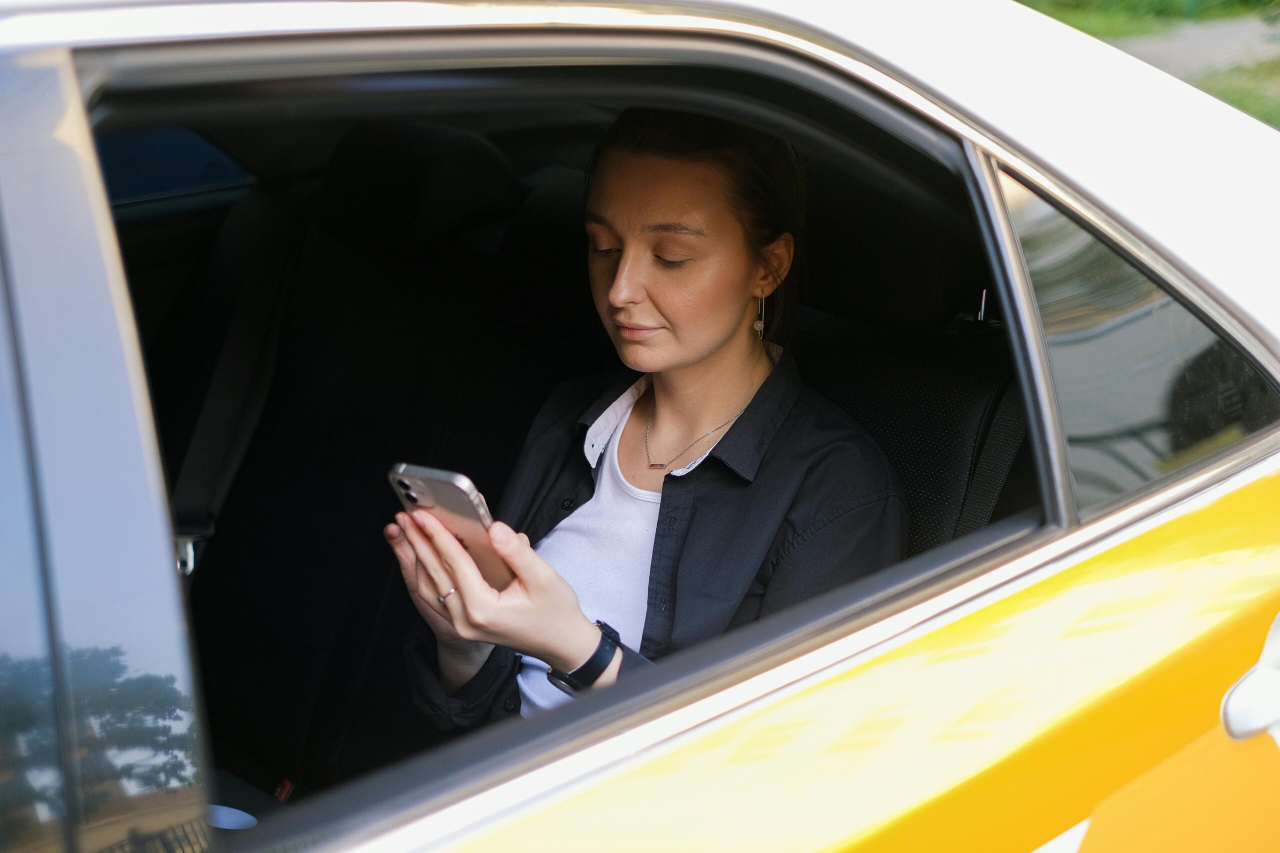 A woman in a taxi, engaged with her smartphone, symbolizing modern remote work culture.